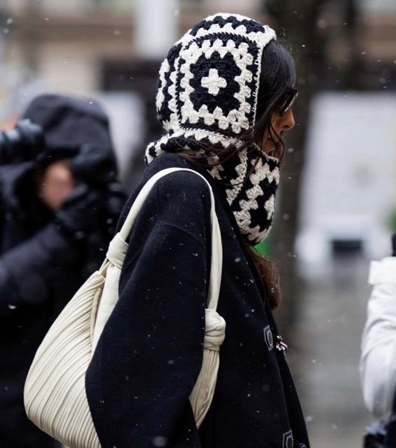 Kvinde i sort frakke med hvid og sort granny square balaclava